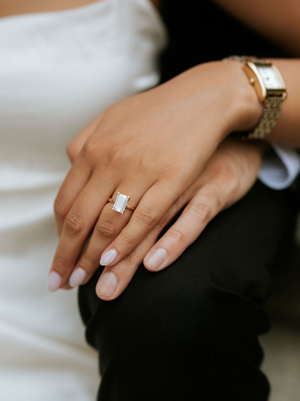 A close-up sequence of hands wearing an elegant emerald-cut diamond engagement ring on a white and black background.