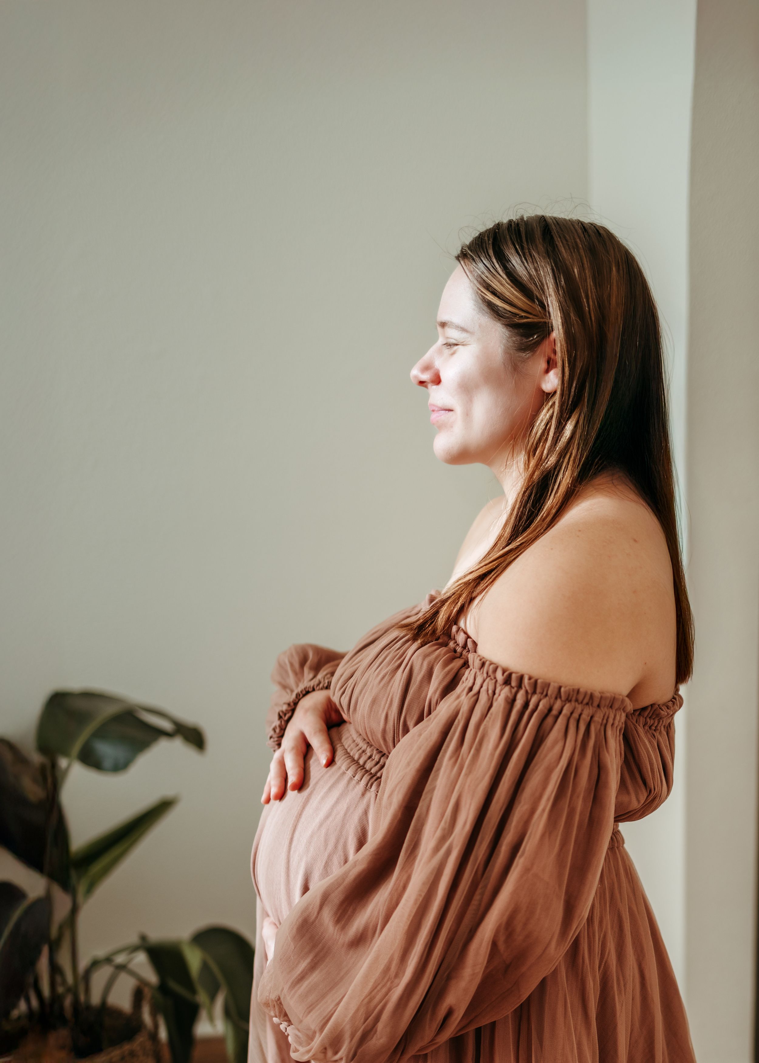 An off-shoulder brown dress is showcased in a minimalist interior setting with natural lighting.