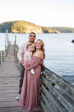 A family shares tender moments on a wooden pier overlooking a scenic bay at sunset.