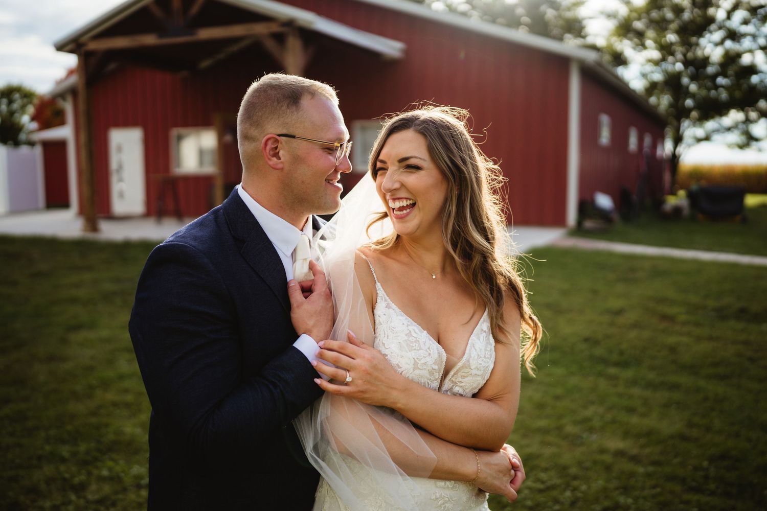 Newlyweds embracing in front of a red barn on a sunny wedding day.