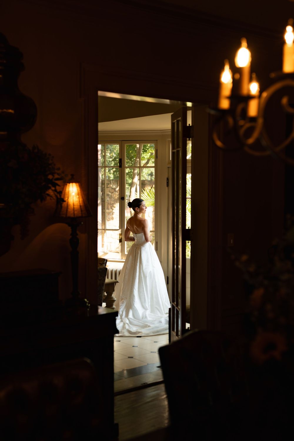 Silhouette of a bride in wedding dress standing in backlit doorway creating dramatic lighting effect.