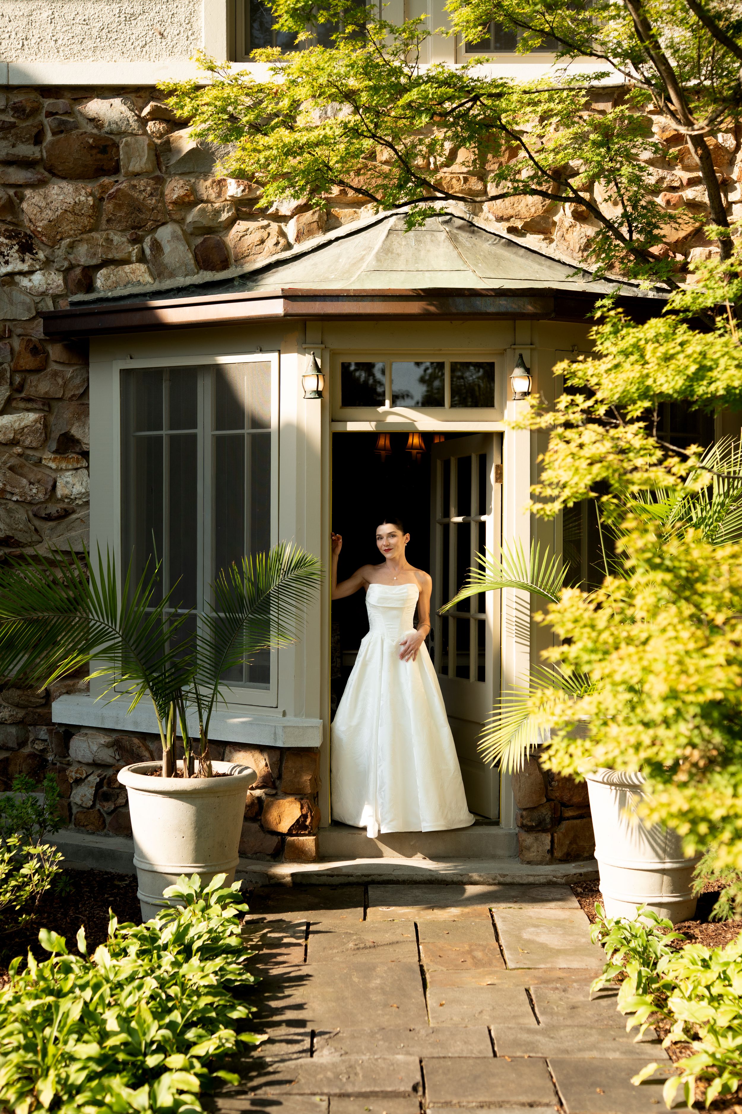 White wedding dress captured in garden setting with stone walls and lush greenery.