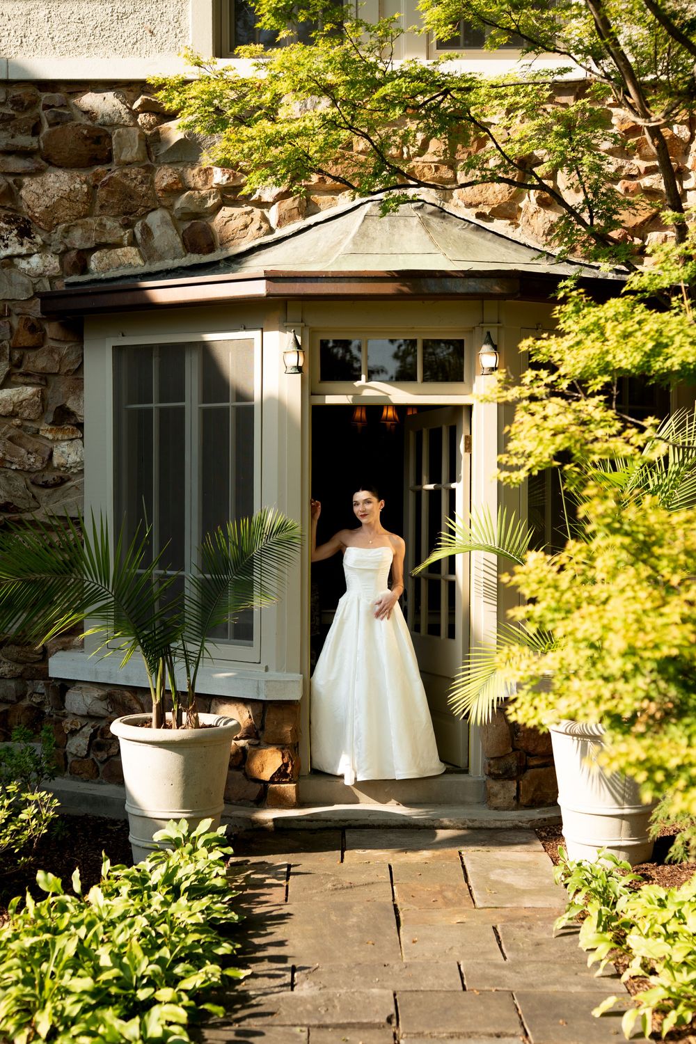 White wedding dress captured in garden setting with stone walls and lush greenery.