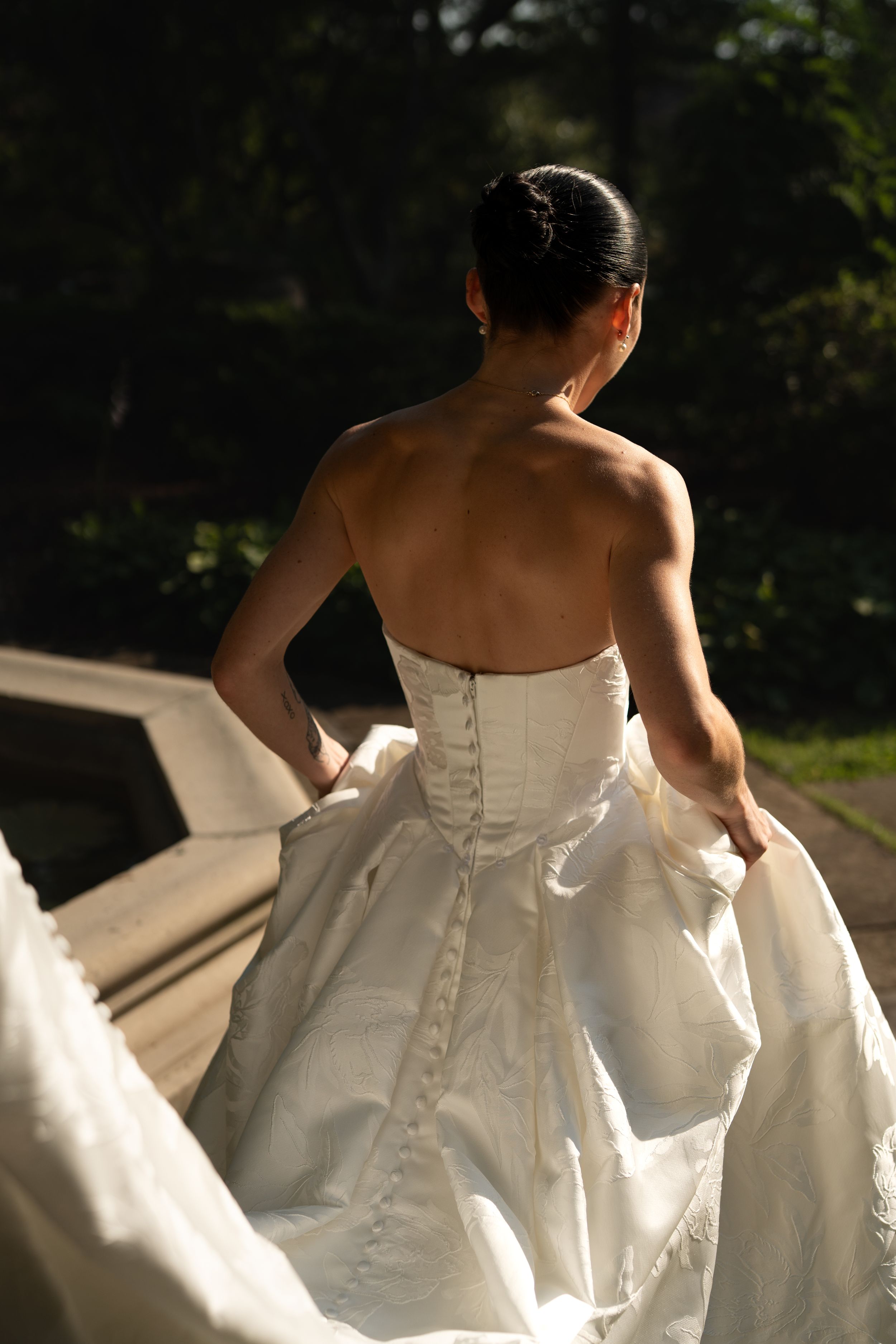Back view of wedding dress details showing intricate buttons and fabric in sunlight.