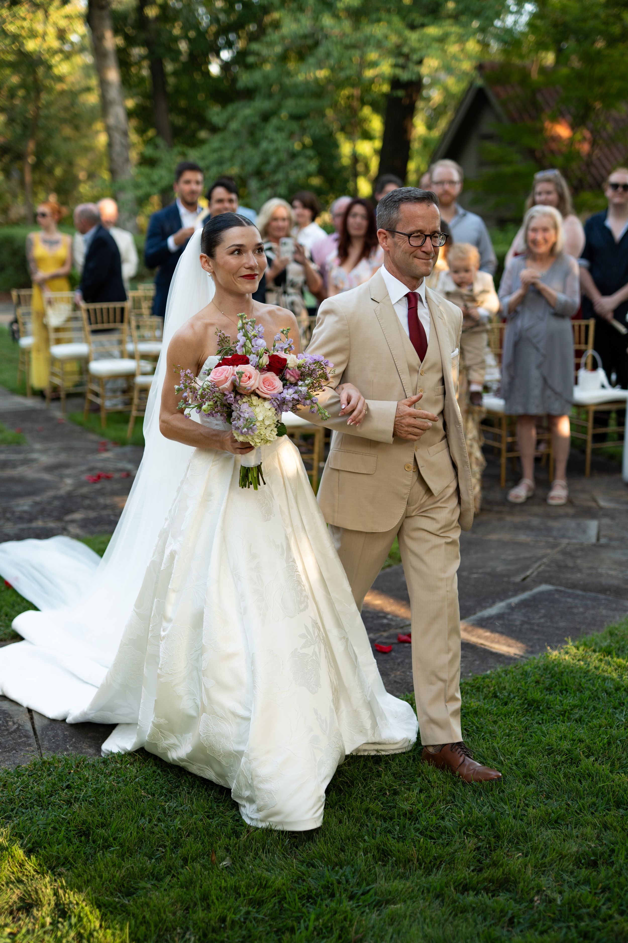 Wedding party walks along a stone path during an outdoor summer celebration.
