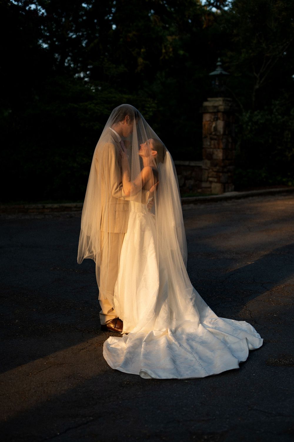 Dramatic silhouette of a wedding dress and veil captured at dusk.