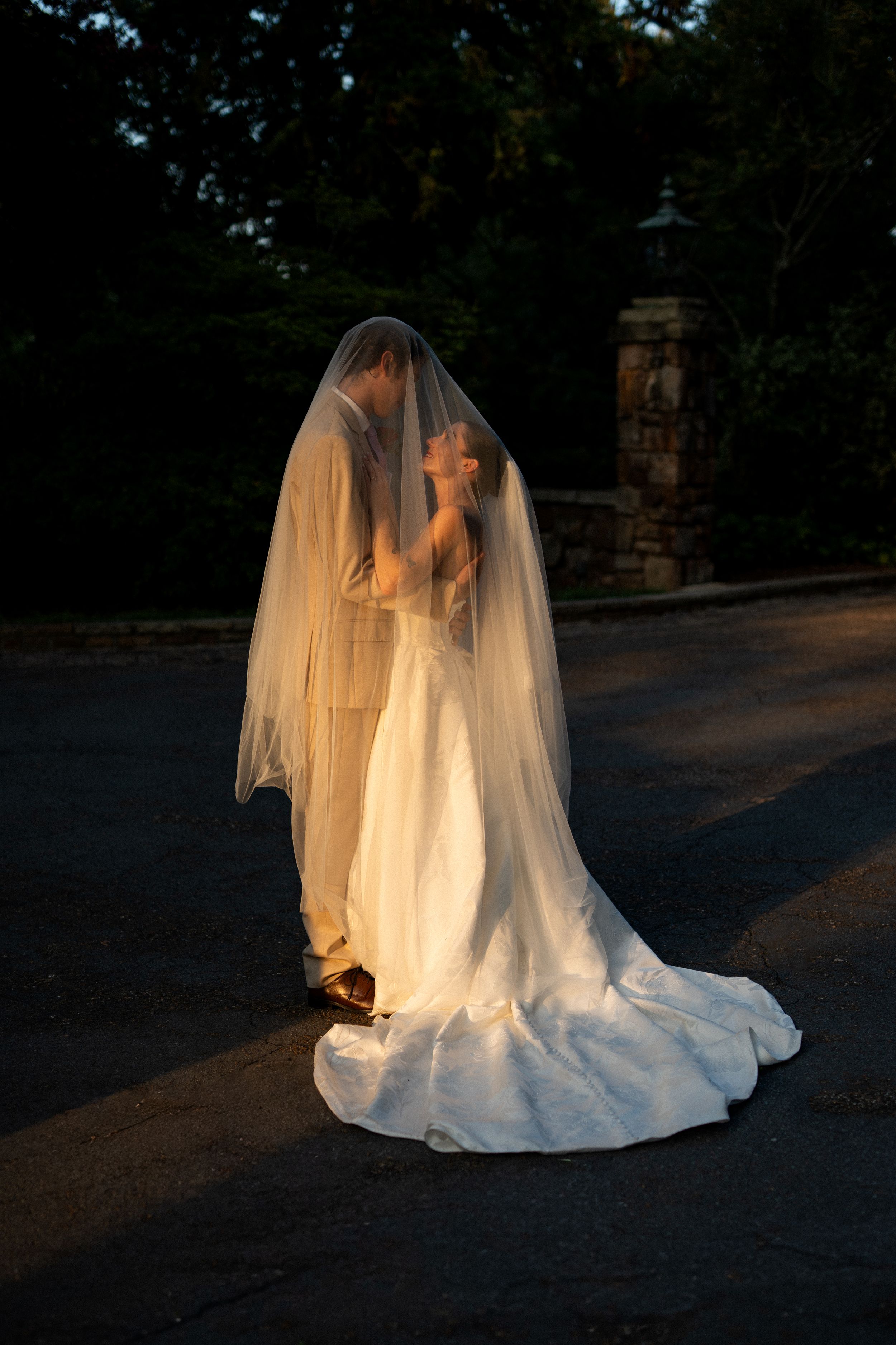 Dramatic silhouette of a wedding dress and veil captured at dusk.