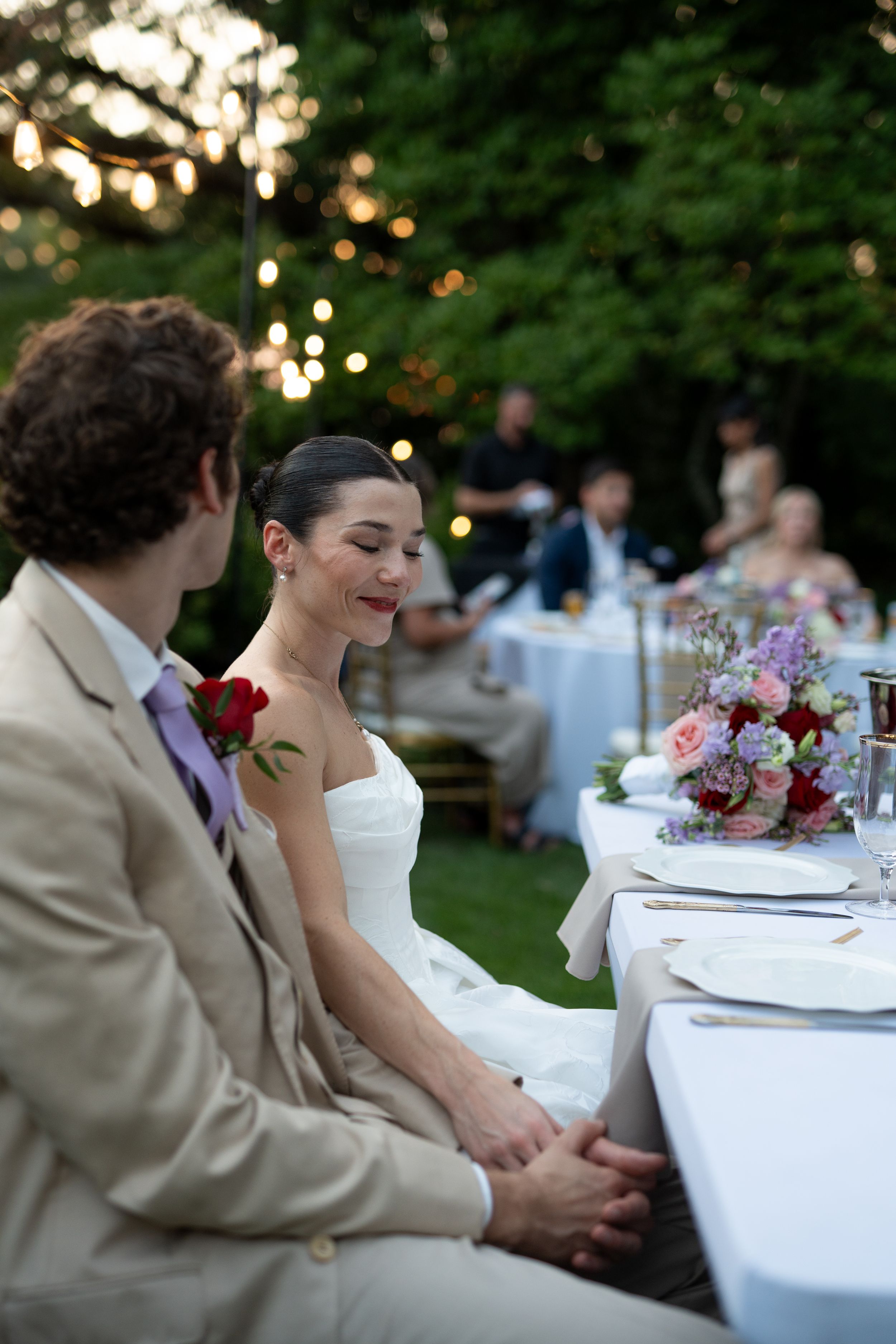 Outdoor wedding reception with white tablecloths and string lights at dusk.