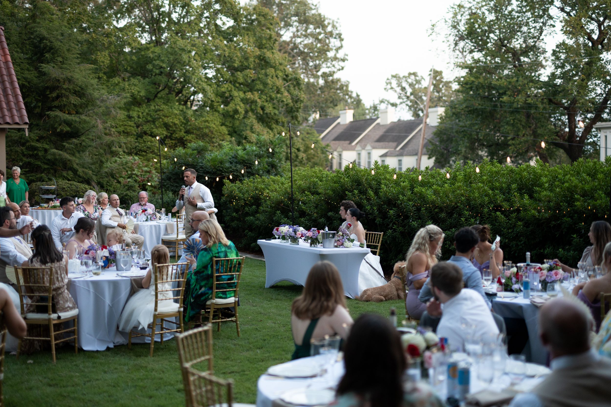 Garden wedding reception setup with tables and chairs under trees.