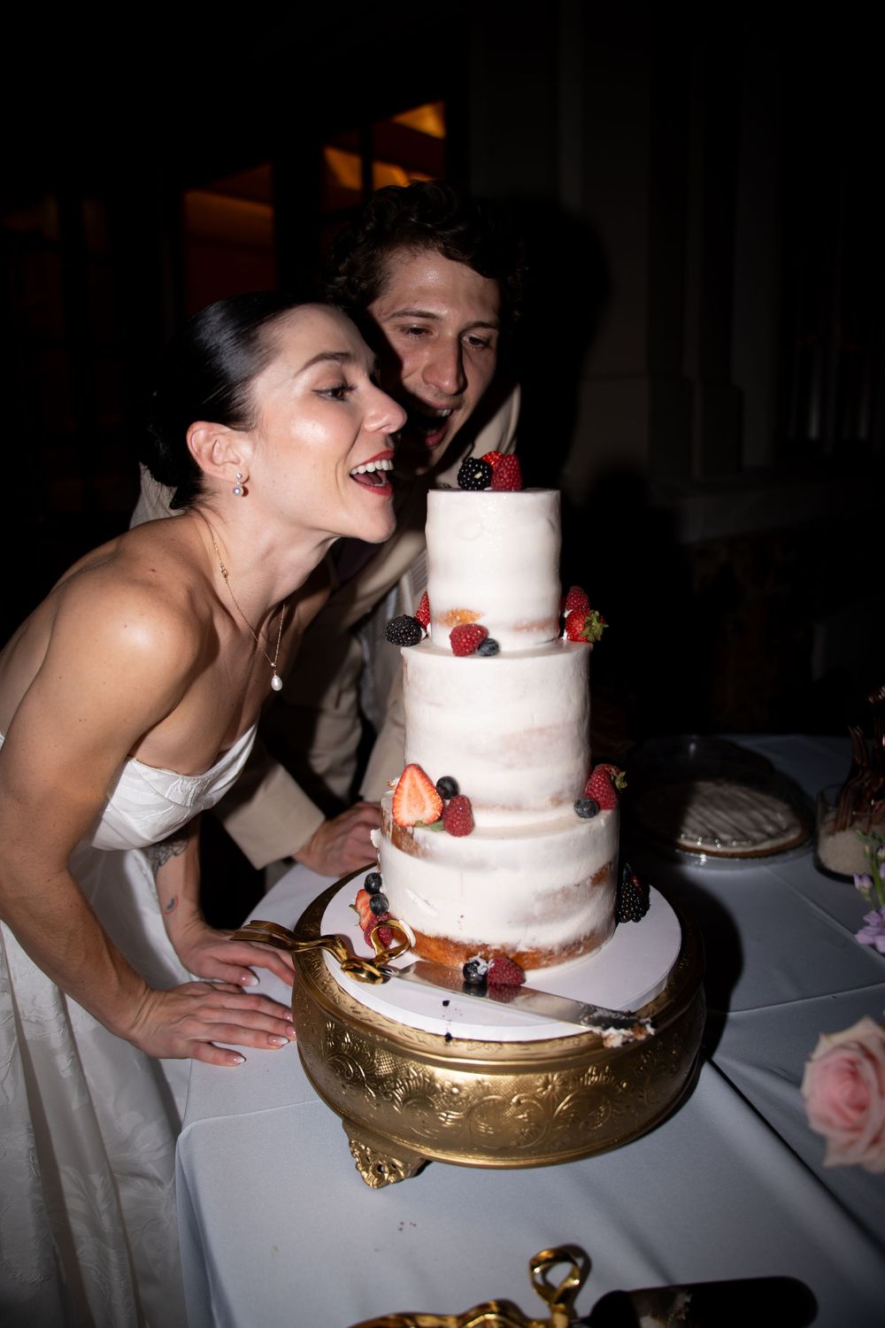 Wedding couple interacting playfully with their white tiered wedding cake.