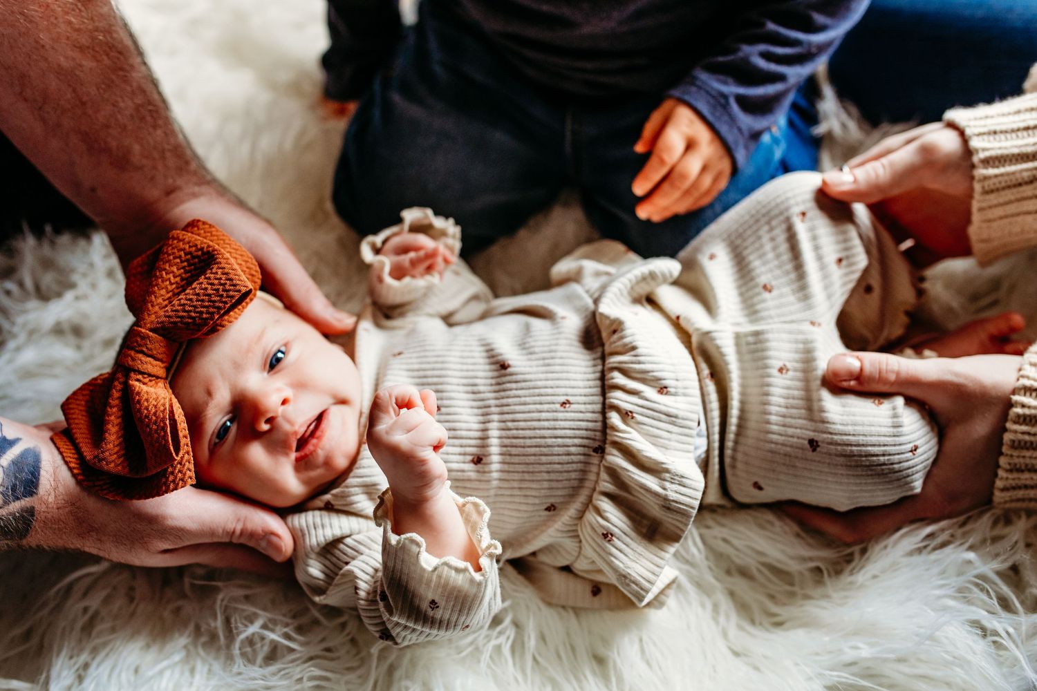 An artistic baby portrait showing the hands of all family members holding the baby.