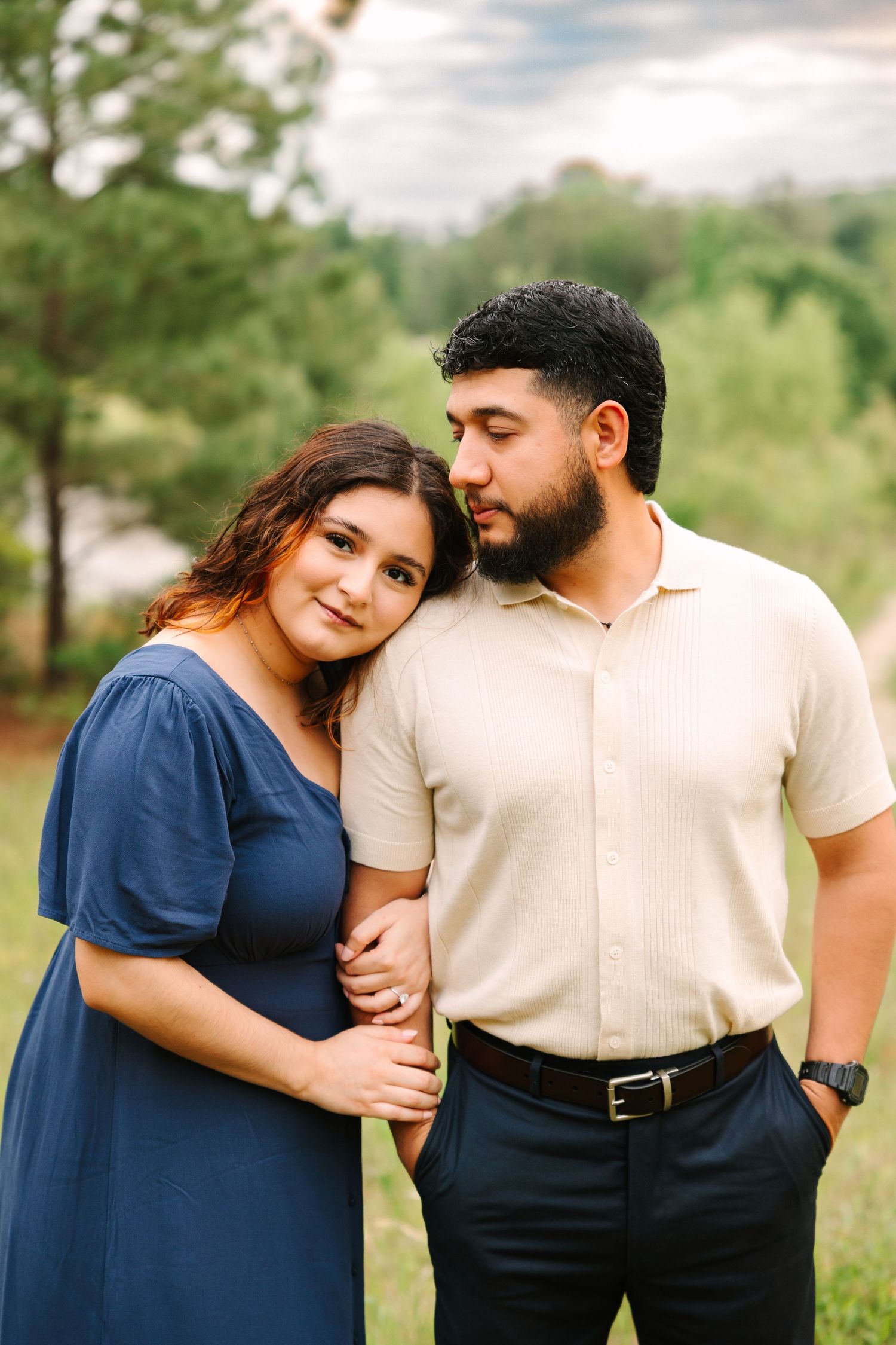 A couple in coordinating navy and cream outfits embrace while posing outdoors in a natural setting during a photo session.