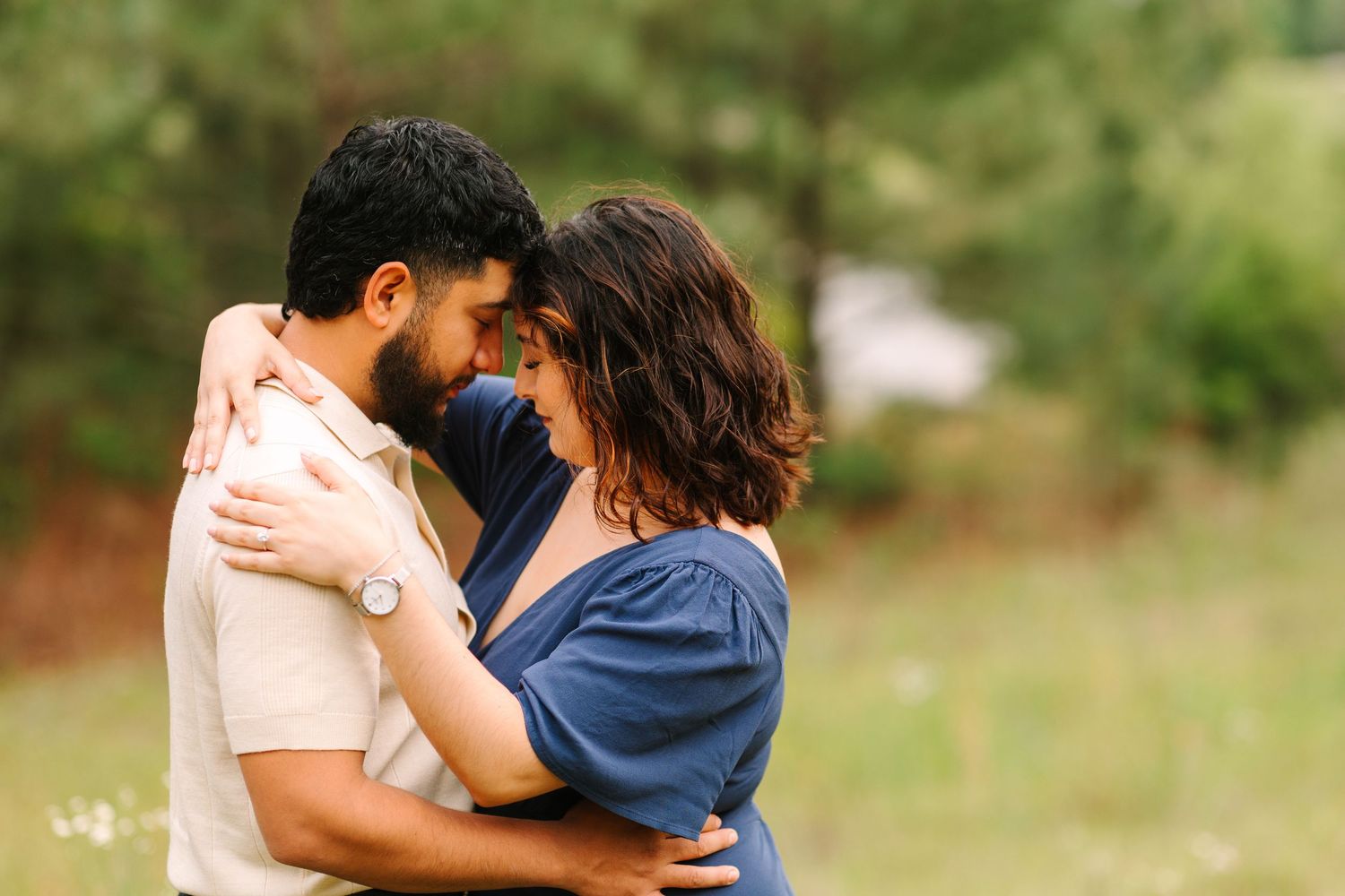 Romantic couple embraces in a sunny meadow wearing coordinating blue and beige outfits.