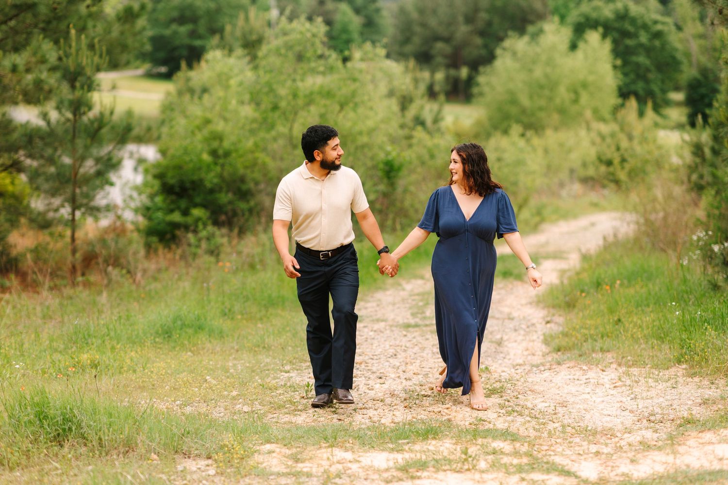 Couple walking hand in hand down a nature path surrounded by lush greenery.
