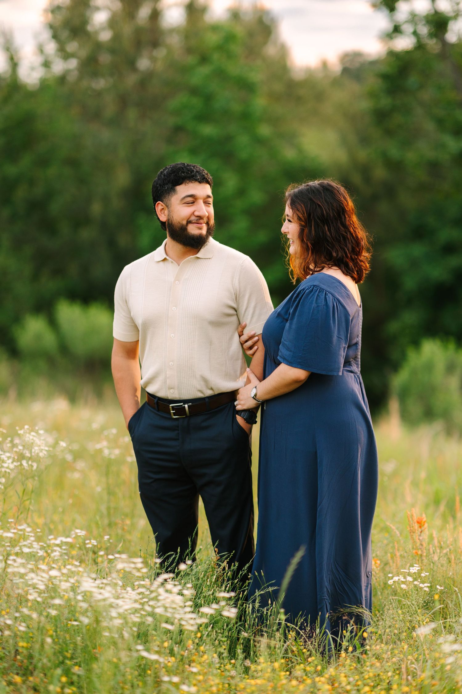 A tender moment between a couple standing in a meadow with wildflowers and green trees.