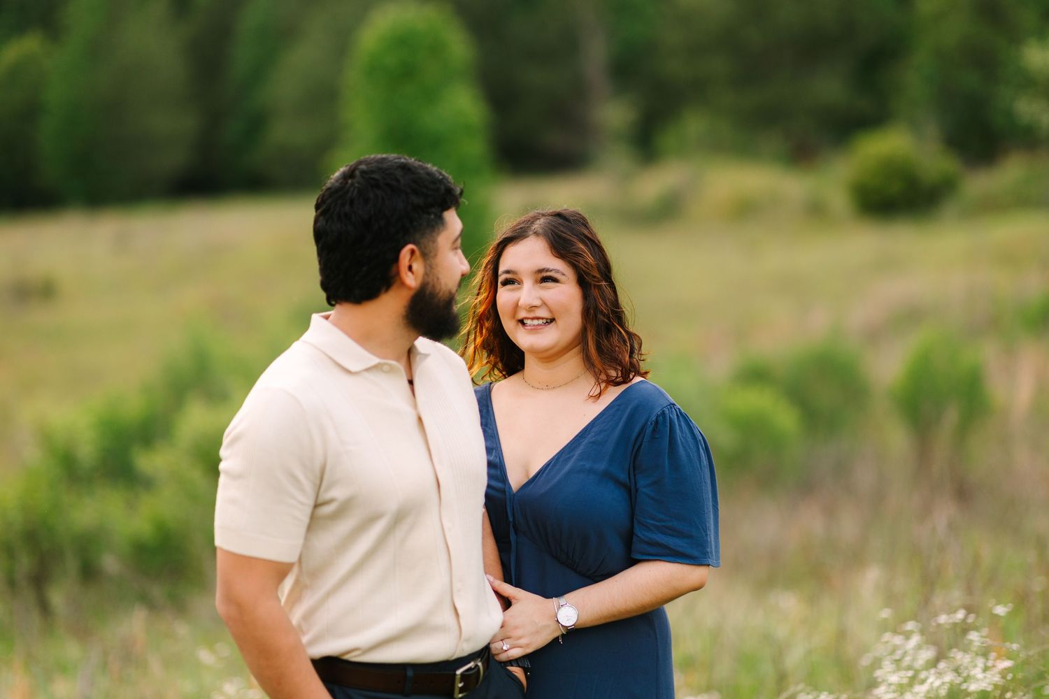 A couple shares a joyful moment together in an outdoor meadow setting with green hills in the background.