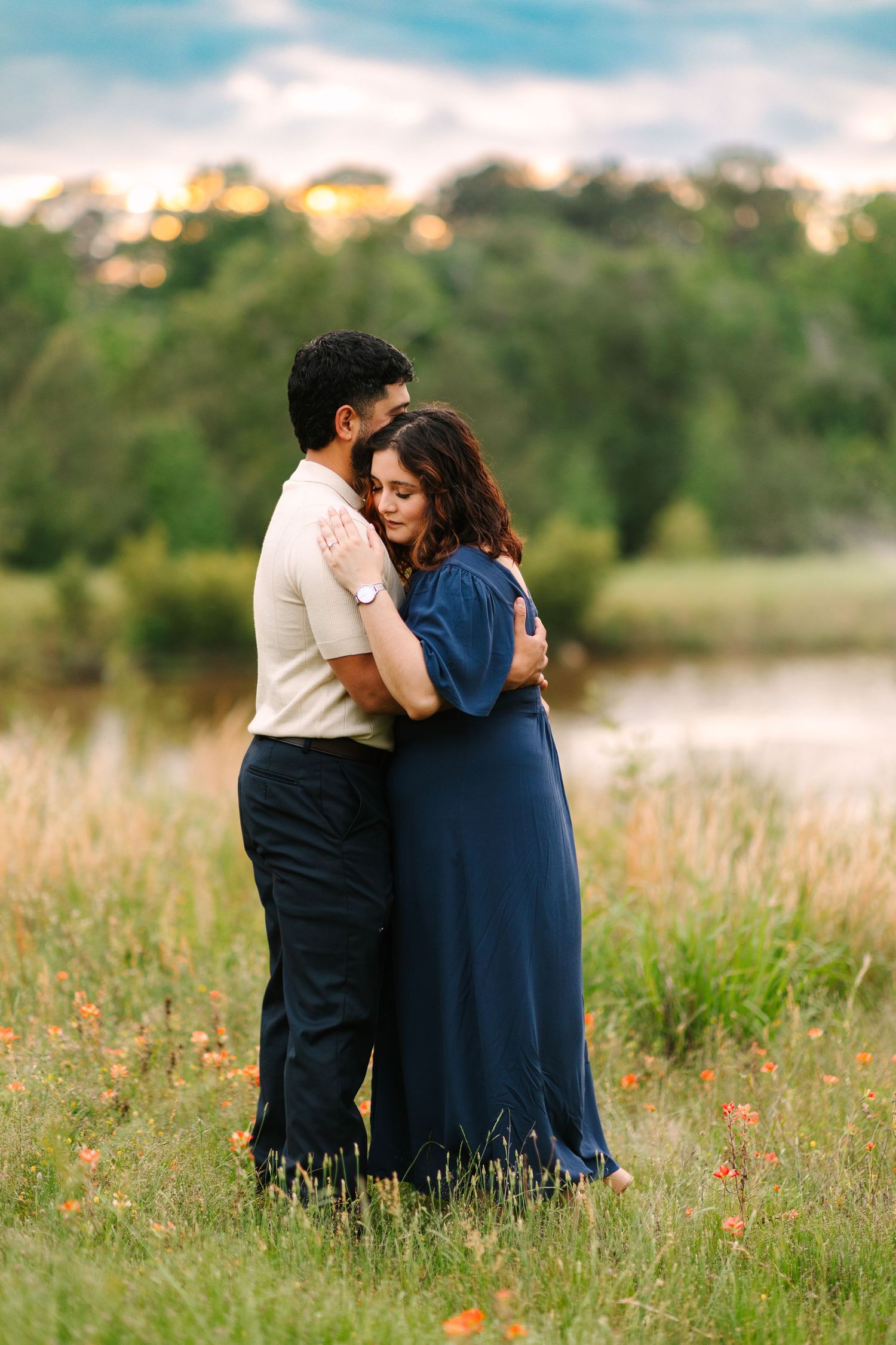 A couple sits together intimately in a sunlit meadow with wildflowers during golden hour.