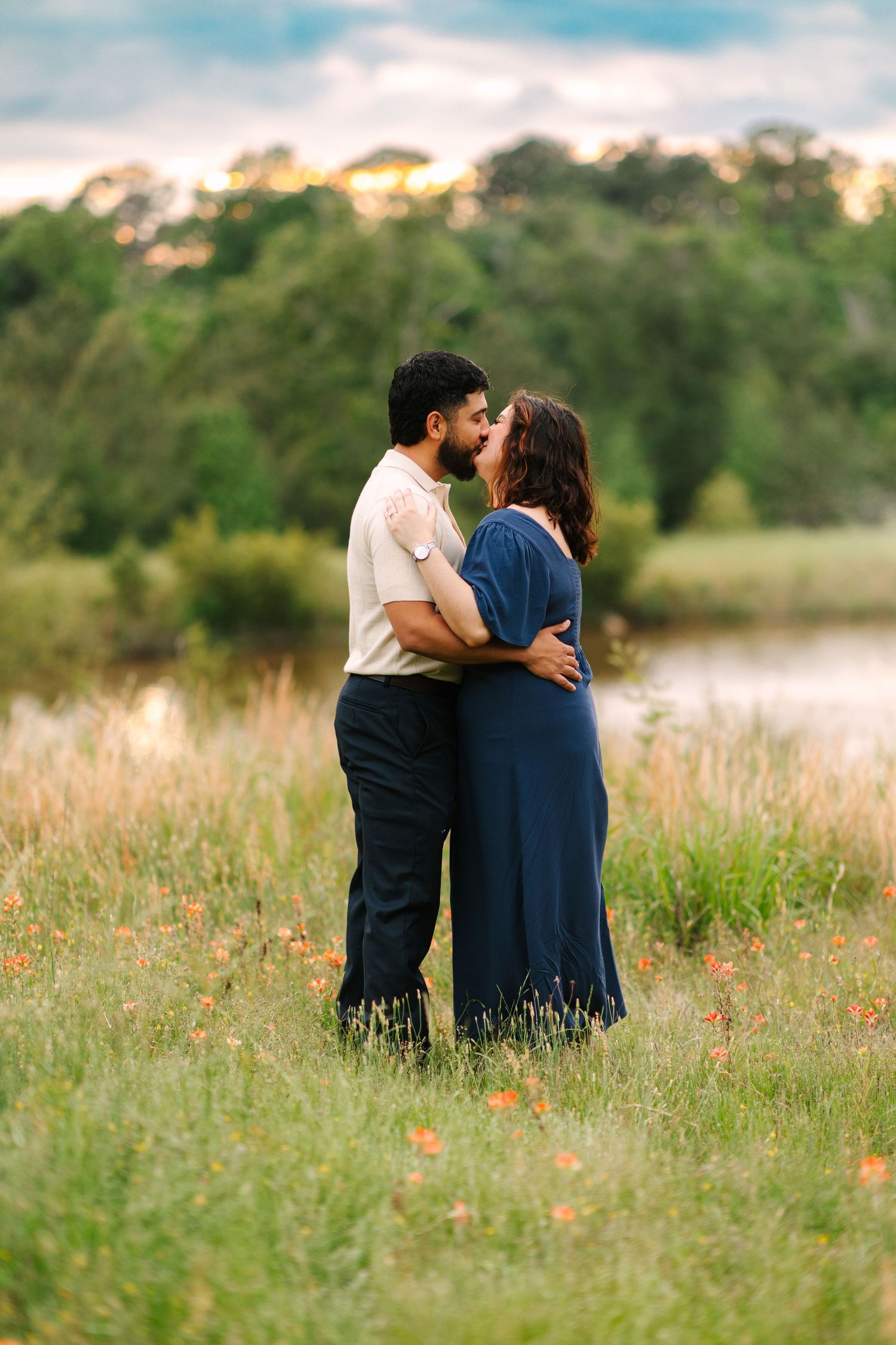 A couple embraces romantically in a wildflower meadow at sunset with soft golden lighting and natural scenery.