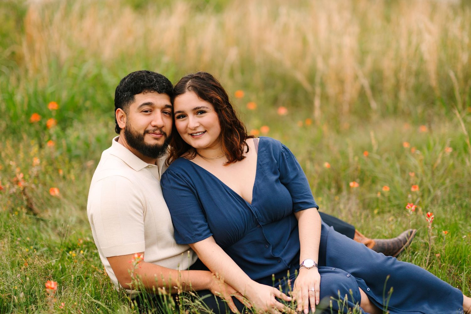 Couple sitting together in a wildflower meadow wearing coordinated blue and beige outfits.