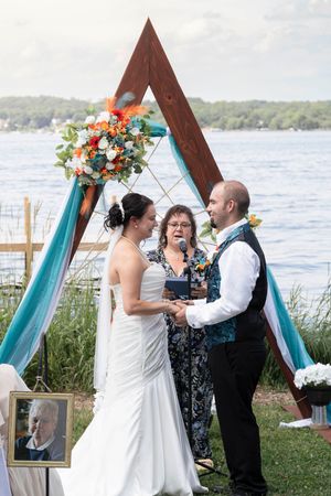 Lakeside wedding ceremony under wooden arch decorated with turquoise fabric and coral flowers.