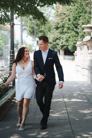 Couple walking together on tree-lined pathway in formal attire.