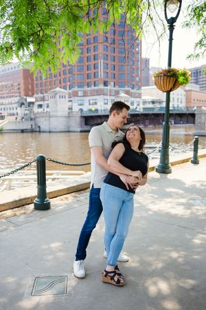 Romantic couple moment captured near urban waterfront with city buildings in background.