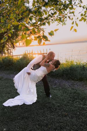 Romantic sunset wedding photos showing couple in dramatic dip pose by the water.