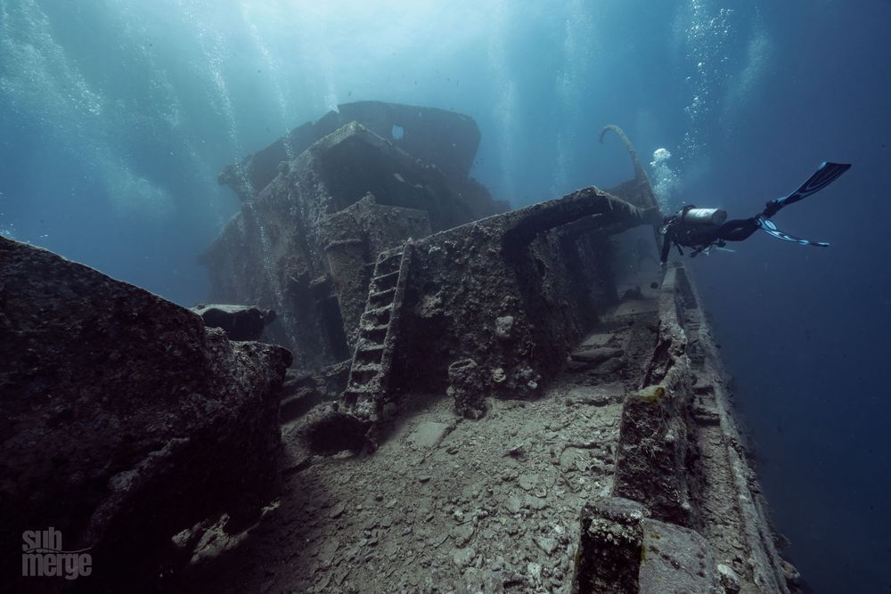 Scuba divers explore vibrant coral reefs and underwater rock formations in crystal clear tropical waters.