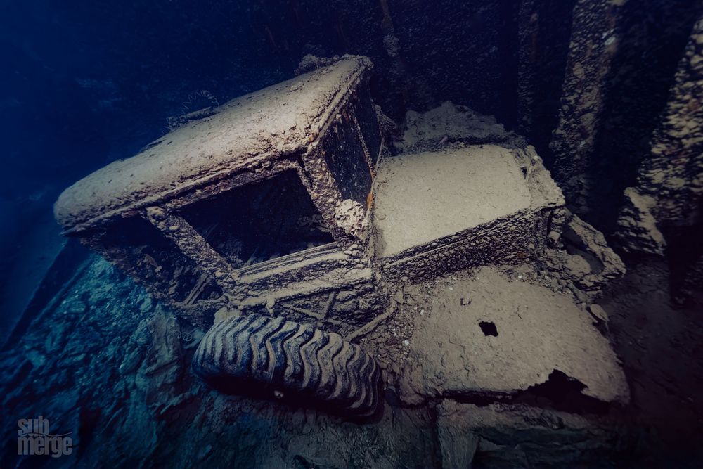 A collection of six wrecked and abandoned cars covered in snow lie in a dimly lit parking area at night.