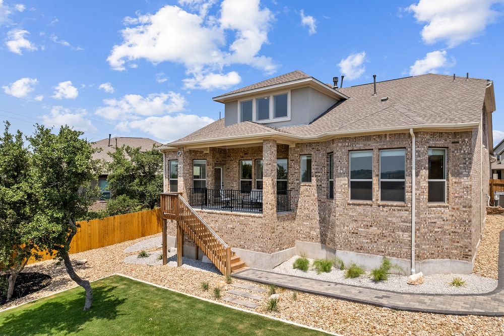 Modern stone and stucco home exterior with large windows and landscaped yard under bright blue sky.