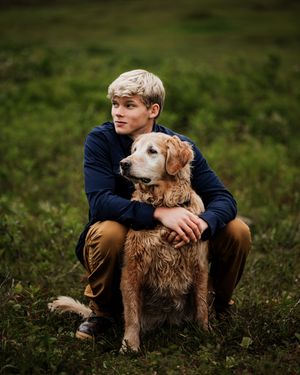 Senior photoshoot with golden retriever in grassy New Hampshire field.