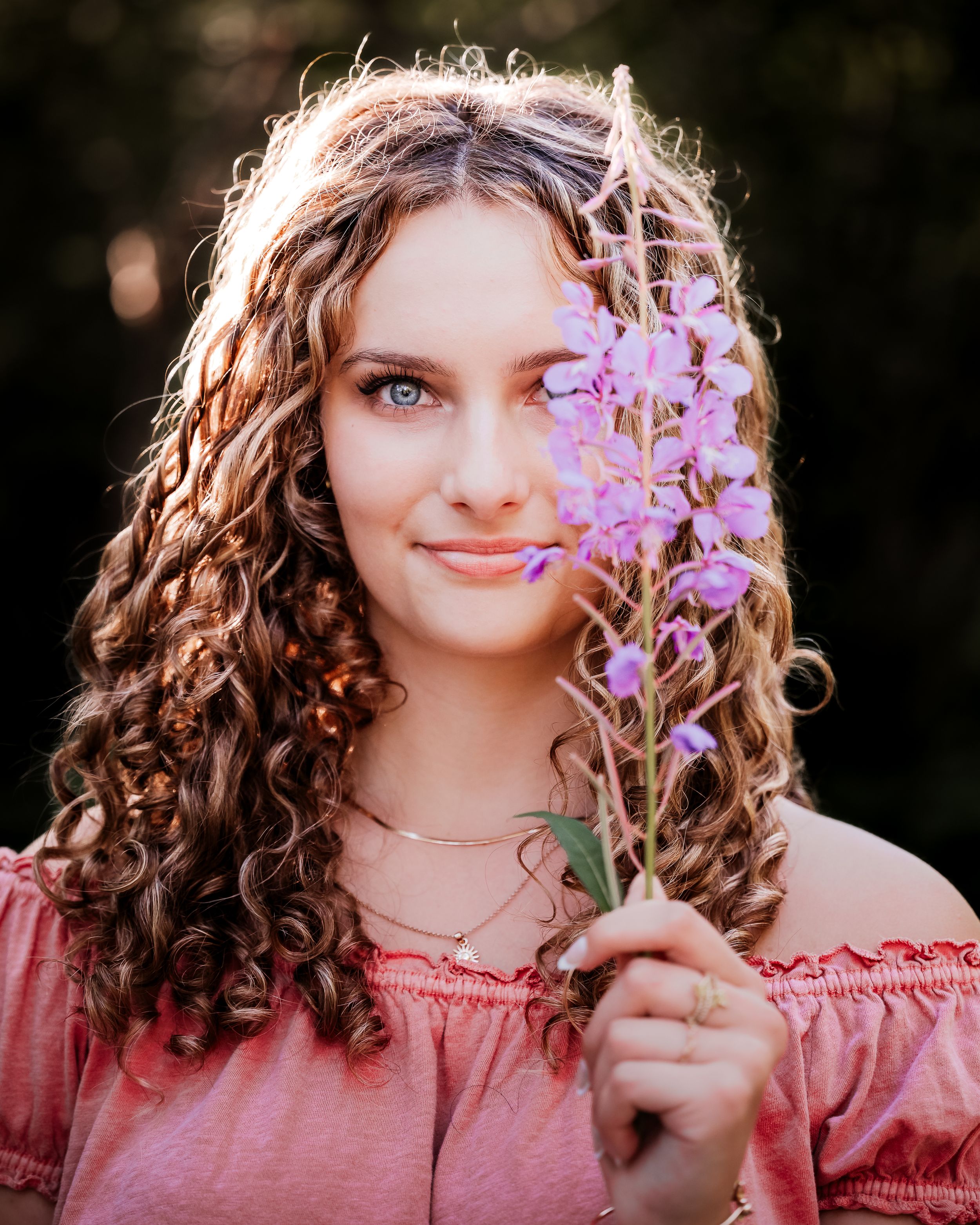 Senior portrait in New Hampshire, girl with curl hair holding purple wildflowers.
