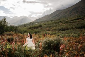 High school senior girl in yellow dress in a field of vibrant red wildflowers with majestic mountains in the background during golden hour.