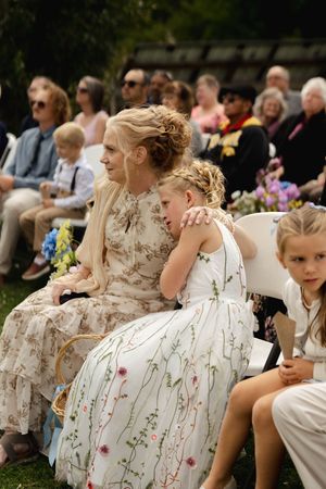 Wedding guests seated outdoors wearing coordinated floral dresses in soft neutral tones.