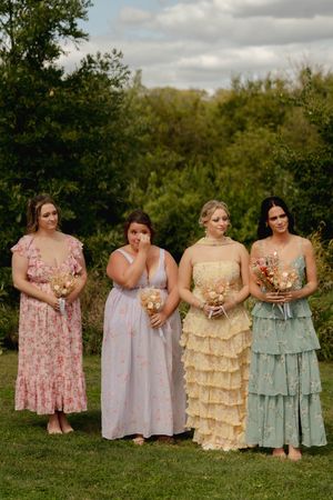 Wedding party members pose in pastel vintage-inspired dresses holding matching bouquets.