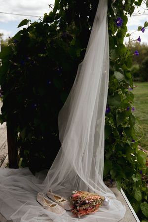 Wedding veil and floral bouquet artistically arranged against green foliage backdrop.