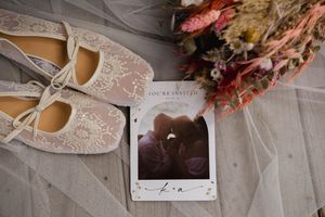Wedding accessories including shoes and flowers arranged on white lace fabric.