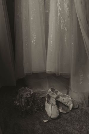 White ballet slippers rest delicately against sheer curtains in ethereal lighting.