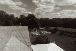 Black and white landscape photograph of cloudy sky over rooftops and trees.