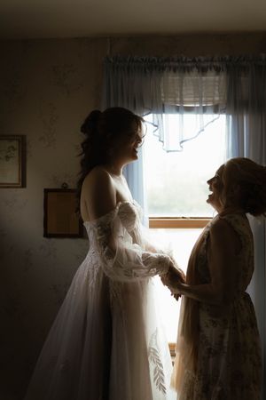 Wedding preparations in a dimly lit room with a flowing white dress and delicate moments being captured.