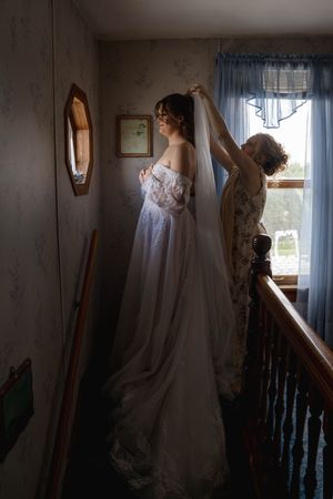 Silhouettes in a room with natural window light highlighting a wedding dress and preparations.
