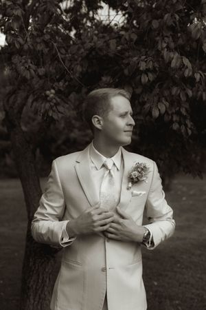 Dramatic black and white portrait of a groom in a light colored suit outdoors.