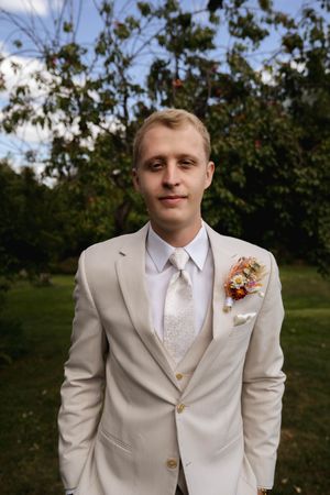 Wedding portrait in a cream suit with boutonniere against a backdrop of fruit trees.