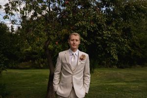 Elegant wedding portrait in a light suit standing among orchard trees.