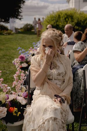Guests seated outdoors at a wedding ceremony with pink and purple flowers in the background.