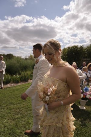 Wedding party members pose together outdoors under cloudy skies during a summer celebration.