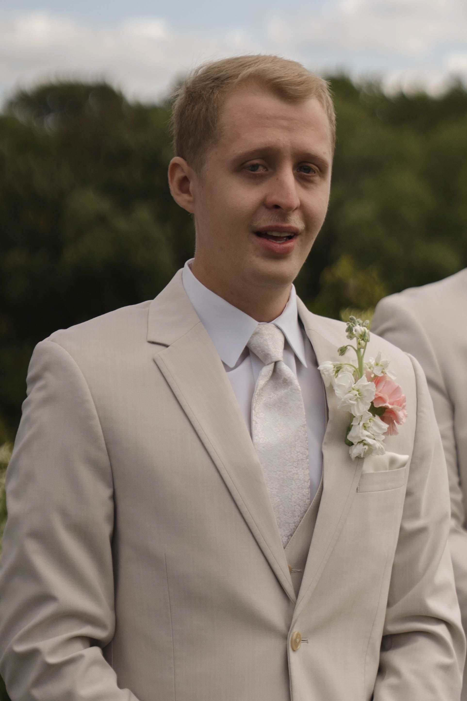 Groomsmen in light beige suits with pink floral boutonnieres smile during outdoor wedding portraits.