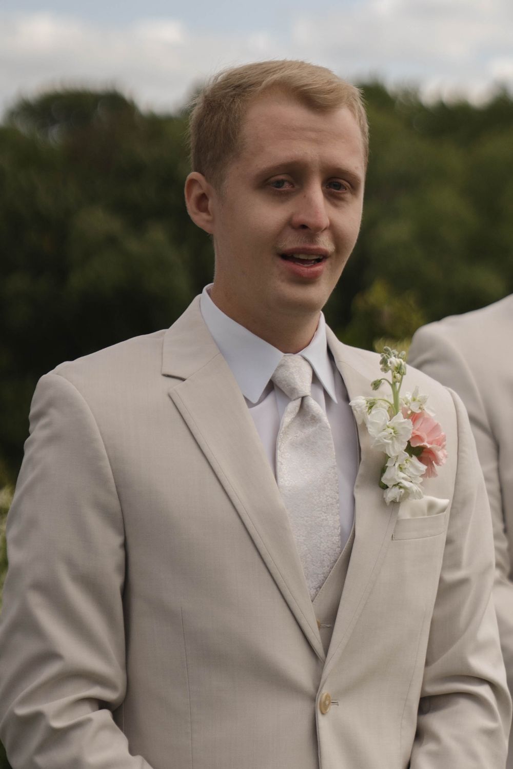 Groomsmen in light beige suits with pink floral boutonnieres smile during outdoor wedding portraits.