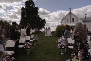 An outdoor wedding ceremony setup with white chairs and floral decorations under a cloudy sky.
