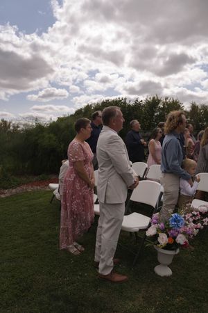 Wedding guests gathering on a grassy hill with white chairs and floral arrangements.